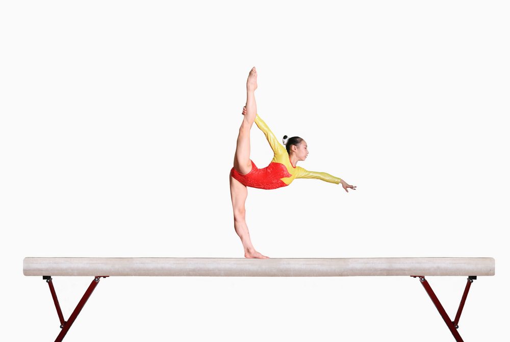 Female gymnast posing on balance beam displaying the laws of physics and how they apply to watching the Olympics