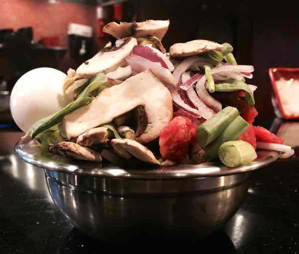 Stainless steel bowl overflowing with food from Mongolian barbecue buffet including mushrooms onions and egg